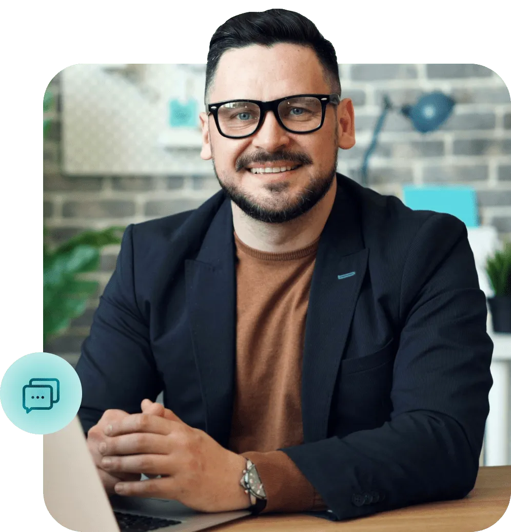 Smiling professional man in glasses and blazer sitting at a desk with a laptop, representing customer support or business communication services